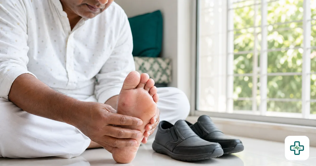 Photorealistic close-up of a person with diabetes inspecting the sole of their bare foot for cuts and blisters in bright daylight, with a pair of soft closed shoes beside them