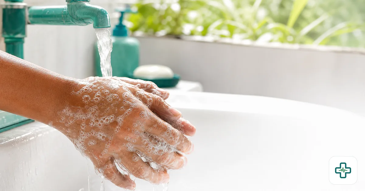 Close-up of soapy hands being scrubbed under clean running water at a tap, with bubbles between the fingers in bright daylight